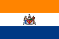 A flag with three equal horizontal stripes colored orange, white, and blue from top to bottom. In the center is the city seal (except for text and circular outline).