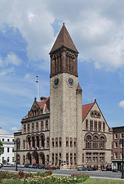 A brown and tan brick building with dark brown trim. The building has a tall bell tower on the nearest corner.